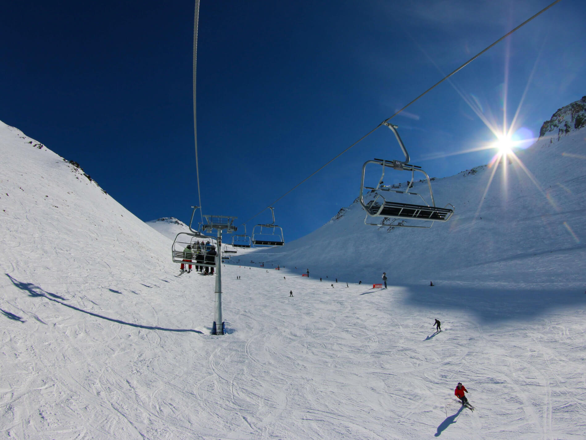 Skiers on a snowy slope with a chairlift overhead under a clear blue sky and bright sun.