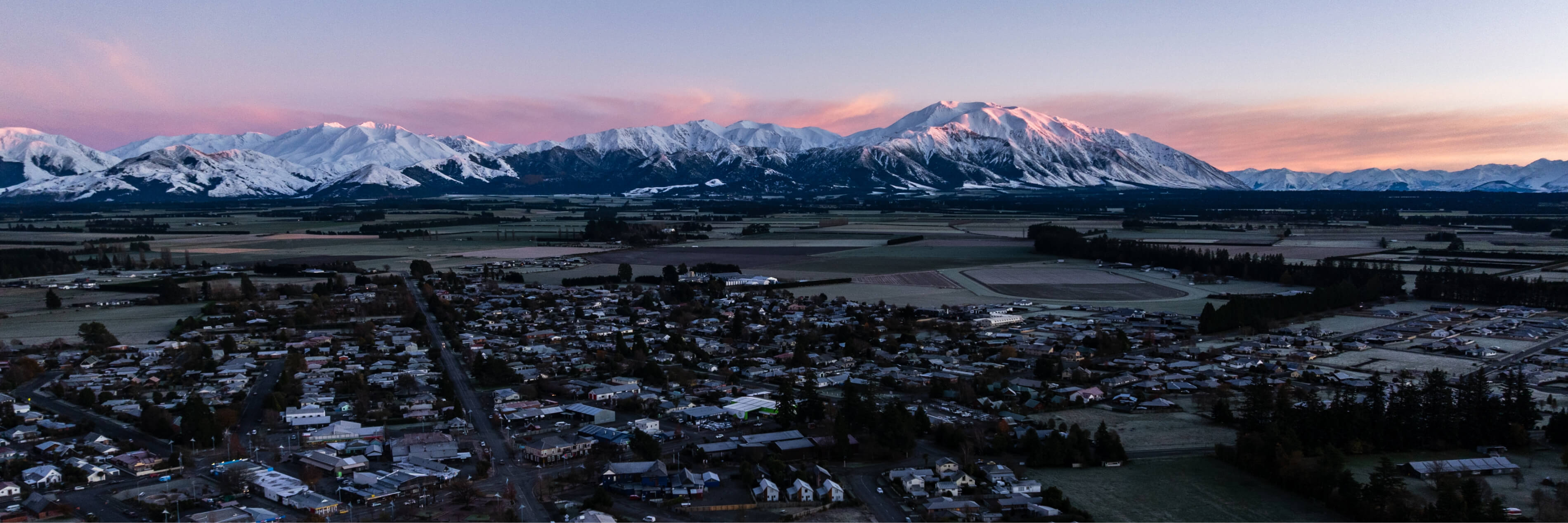 Aerial view of Methven with snow-covered Mt Hutt lit by sunrise in the background.