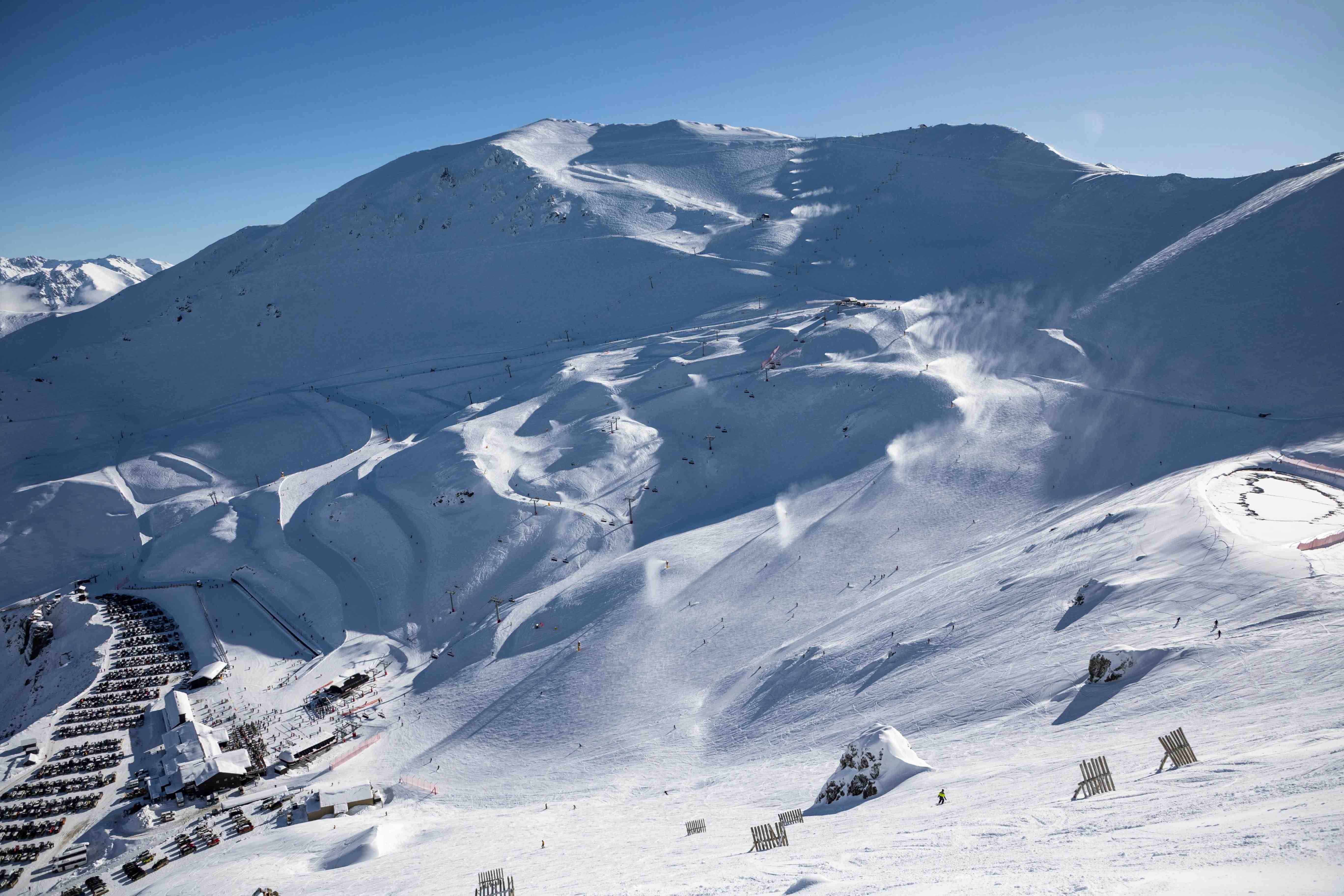 Snowy ski resort on a mountain with ski lifts, skiers, and snow-covered slopes under a clear blue sky.