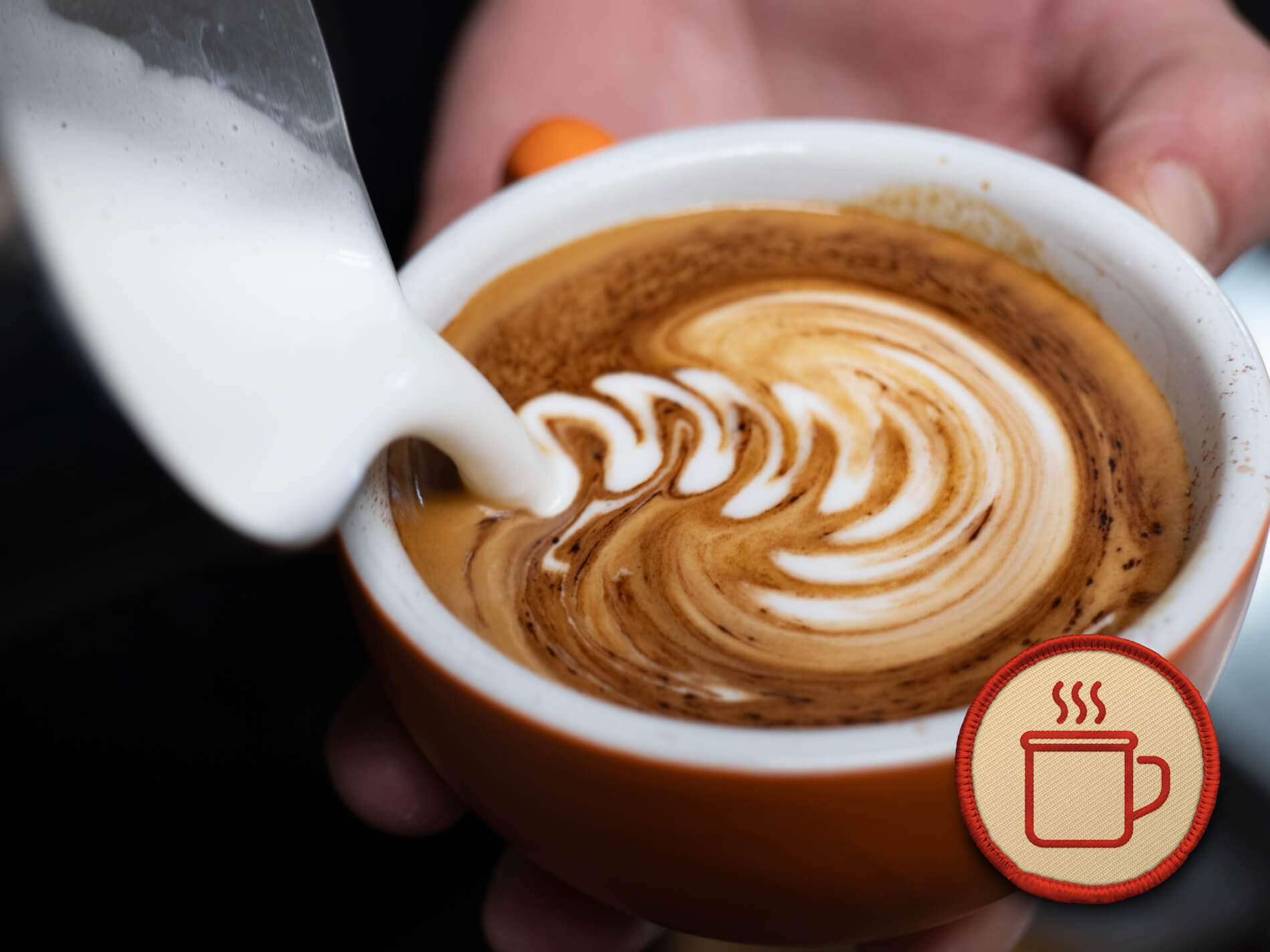 Milk being poured into a cup of coffee creating latte art.
