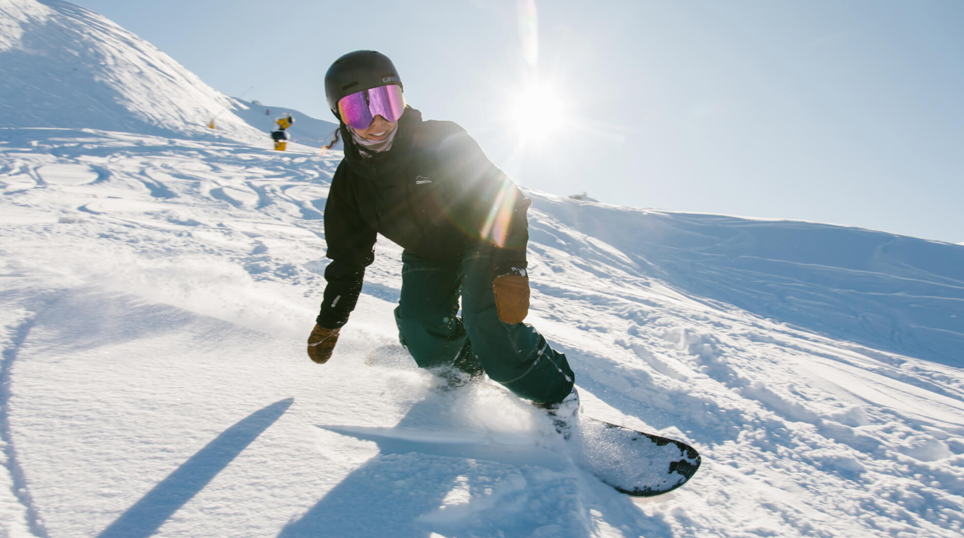 Snowboarder carving a turn on a sunlit slope at Mt Hutt ski field with fresh snow spray