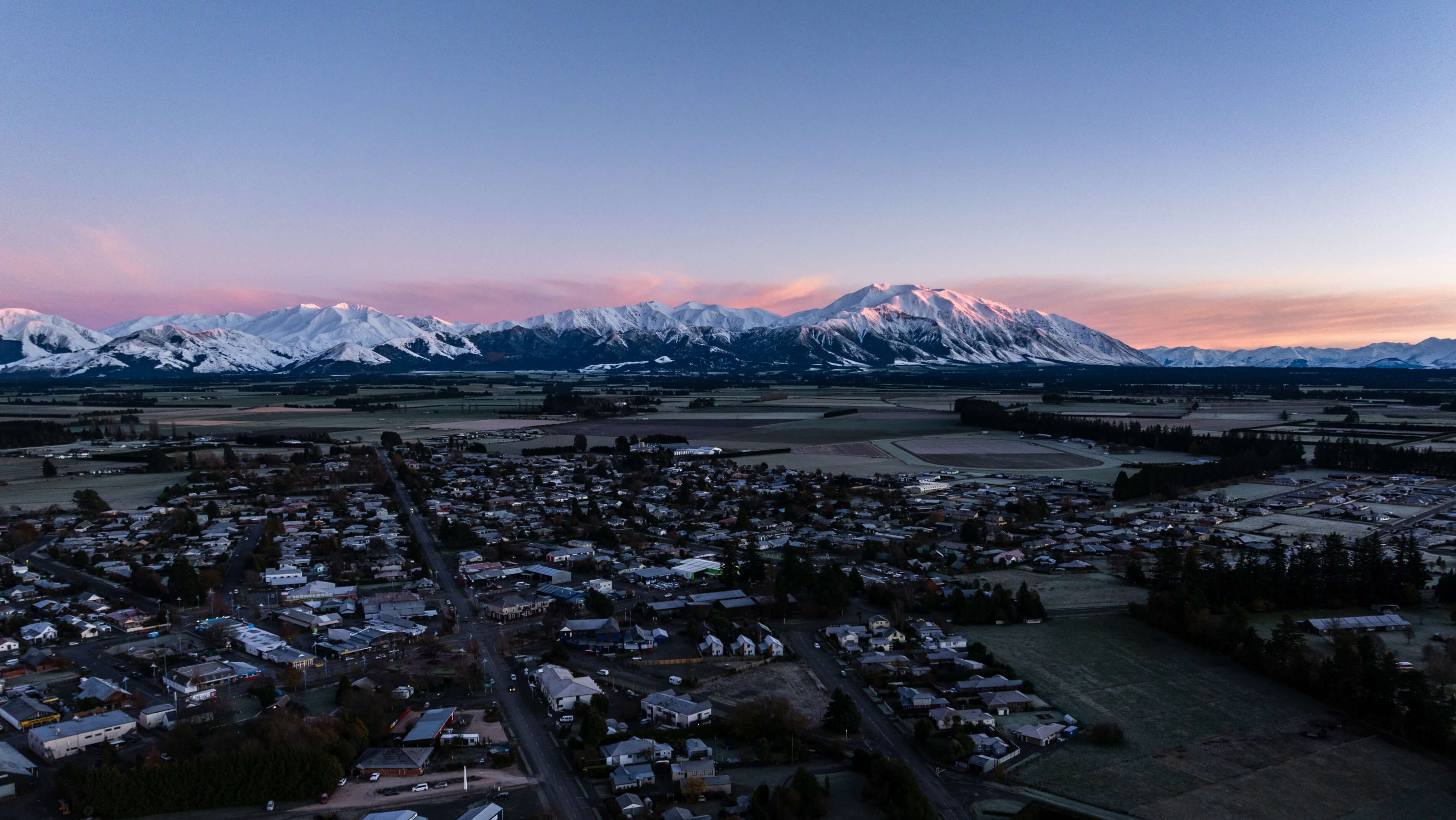 Aerial view of Methven with snow-capped mountains bathed in sunrise light in the background.