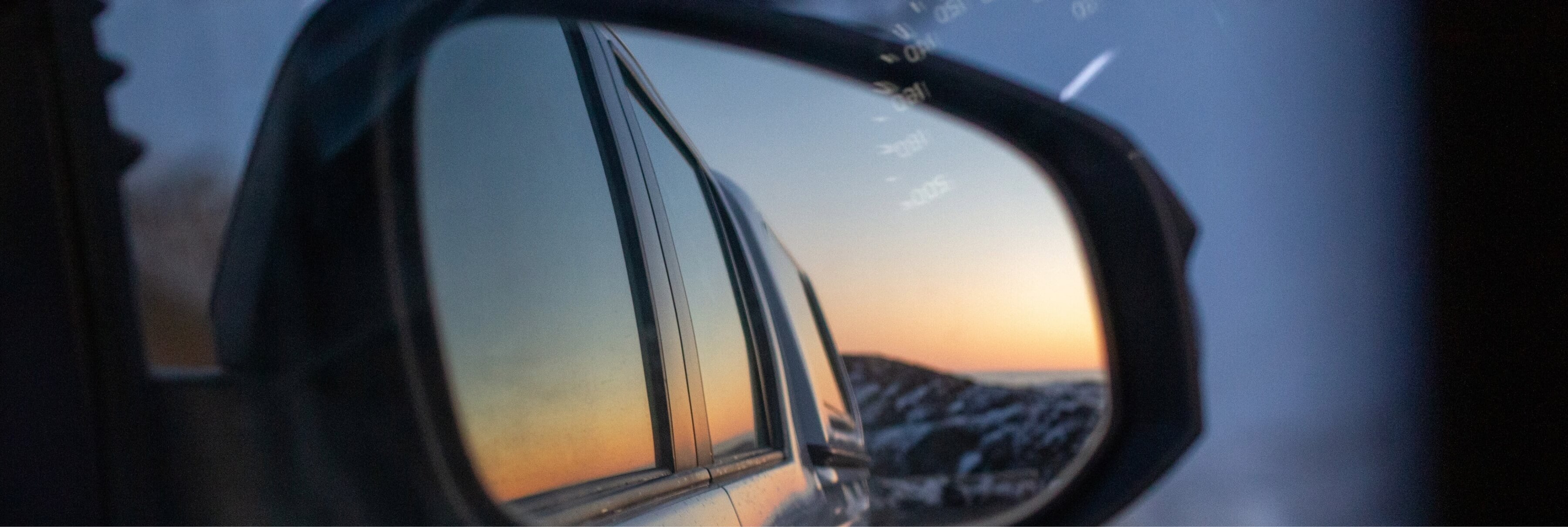 Side mirror of a car reflecting a sunset sky and rocky landscape.