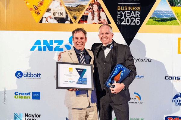 Two men in suits smiling, one holding an award and the other a framed certificate at a business event.