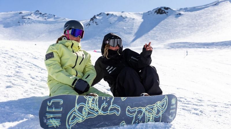 Snowboard instructor pointing out a run to a snowboarder while sitting on the snow at Mt Hutt