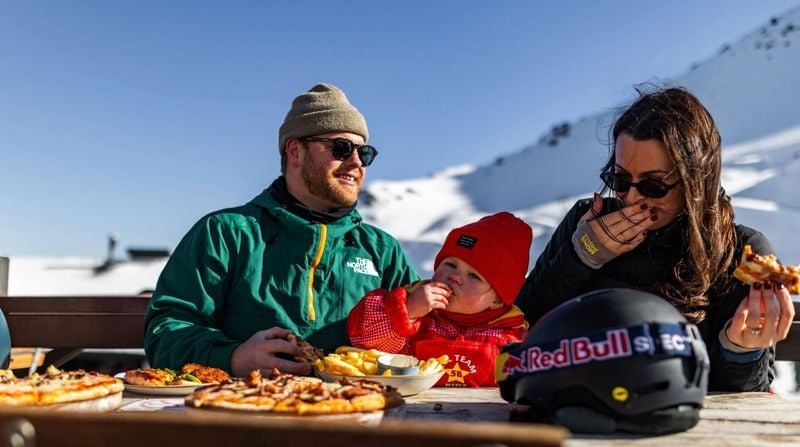 Family enjoying pizza and food outdoors at Mt Hutt ski field with snowy mountain views