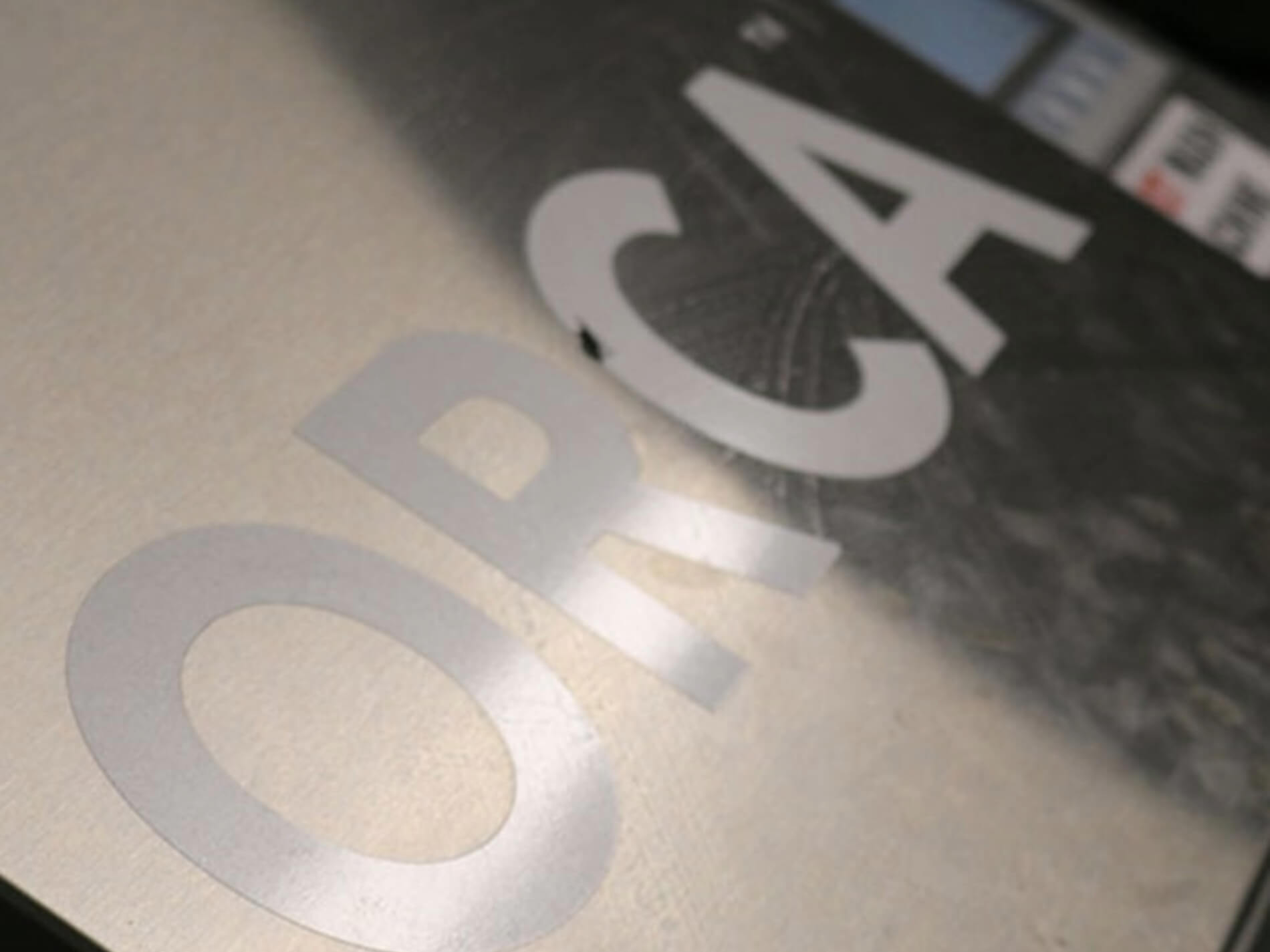 Close-up of a printed surface showing the text 'ORCA' in large, light gray letters on a dark background.