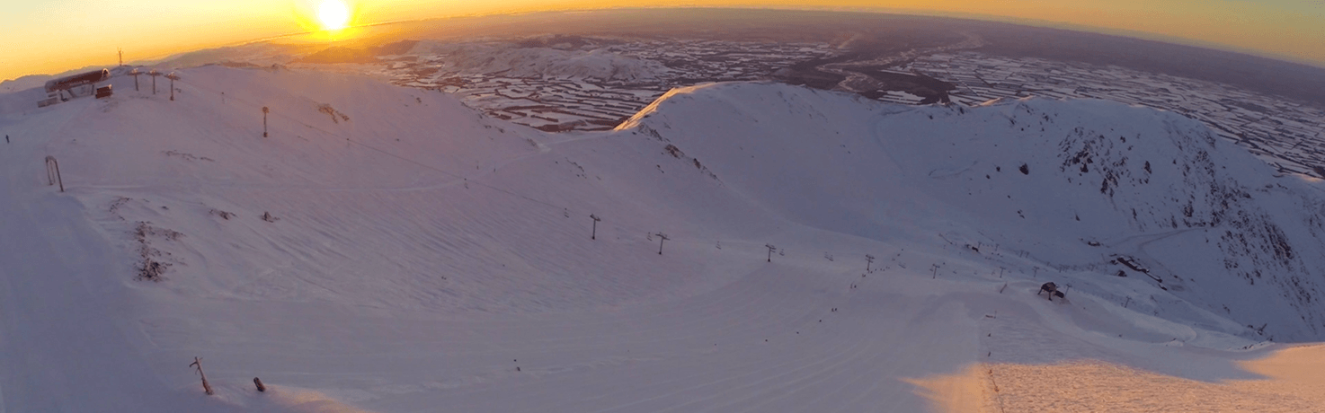Snow-covered mountain ski resort at sunrise with ski lifts and distant valley landscape.