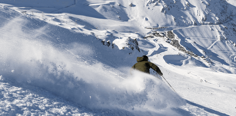Skier carving through fresh powder with wide alpine terrain at Mt Hutt on a clear day