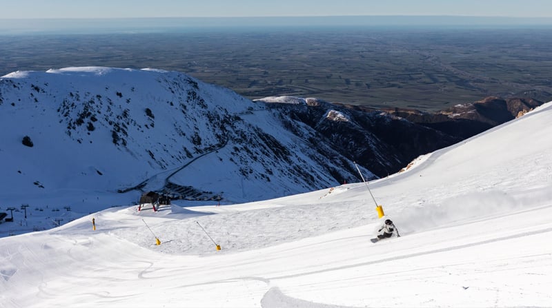 Snowboarder carving down a groomed run at Mt Hutt with views over the Canterbury Plains