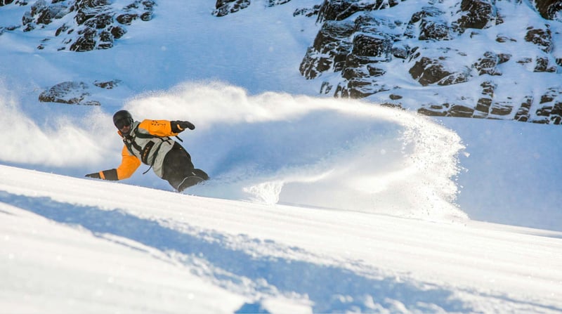 Snowboarder carving through fresh powder snow on a steep alpine slope at Mt Hutt ski field
