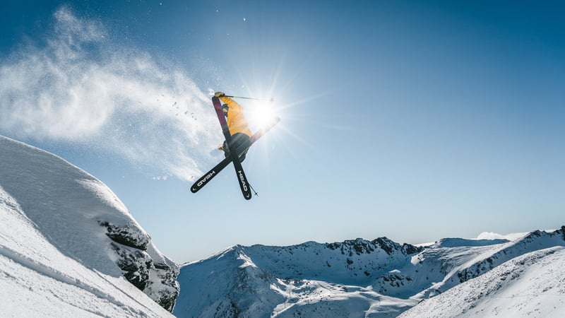 Skier performing a jump with snow spray in alpine terrain at Mt Hutt on a clear day