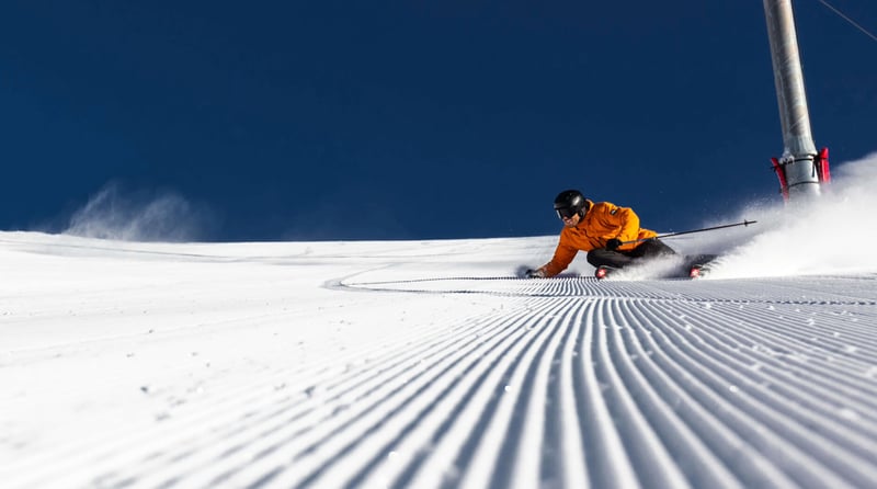 Skier carving a turn on freshly groomed corduroy snow at Mt Hutt ski field under clear blue skies